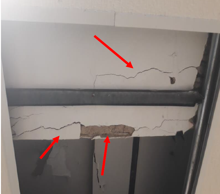 Fissuras em parede próximas a uma viga, indicadas por setas vermelhas.